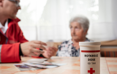 Ein Rotkreuz-Mitarbeiter reicht einer Klientin die Rokreuzdose des Roten Kreuzes Niederösterreich.