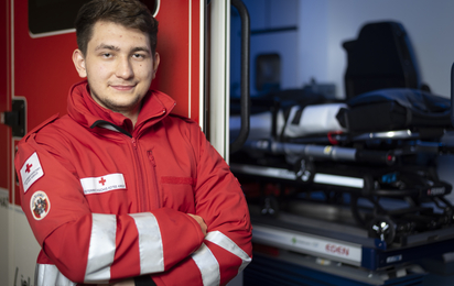 Ein Zivildiener steht mit verschränkten Händen vor einem Rettungsauto.