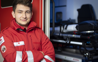 Ein Zivildiener steht mit verschränkten Händen vor einem Rettungsauto.