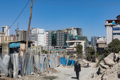 Slums in Addis Abeba, der Haupstadt von Äthiopien. Im Hintergrund sind moderne, neue Gebäude. Ein Mann in Anzug geht die Straße entlang.