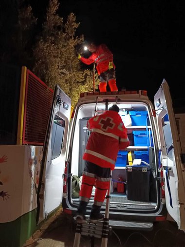 Spanische Rotkreuz-Mitarbeiter mit orangen Rotkreuz-Jacken und Taschenlampen holen im Dunklen Material aus Auto, um nach der Flut zu helfen.