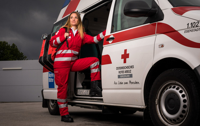 Eine junge Sanitäterin steht in der Tür eines Rettungsautos. Am Rücken trägt sie einen Notfallrucksack.