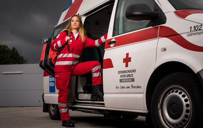 Eine junge Sanitäterin steht in der Tür eines Rettungsautos. Am Rücken trägt sie einen Notfallrucksack.