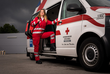 Eine junge Sanitäterin steht in der Tür eines Rettungsautos. Am Rücken trägt sie einen Notfallrucksack.