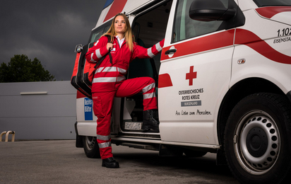 Eine junge Sanitäterin steht in der Tür eines Rettungsautos. Am Rücken trägt sie einen Notfallrucksack.