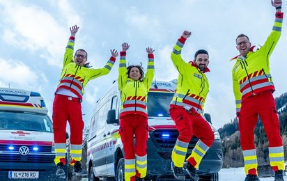 vier Sanitäterinnen springen in Uniform vor einem Auto in die Luft