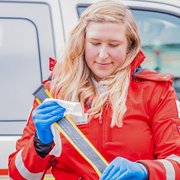 eine junge blonde Frau steht in Rotkreuz-Sanitäteruniform vor einer Trage und putzt die Gute der Trage