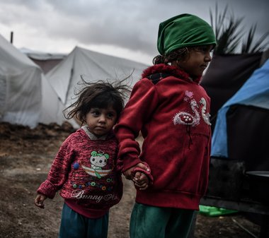 Zwei kleine Kinder stehen Hand in Hand auf schlammigen Boden vor Zelten in Gaza.