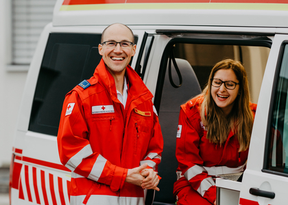 Ein Sanitäter und eine Sanitäterin lachen in die Kamera