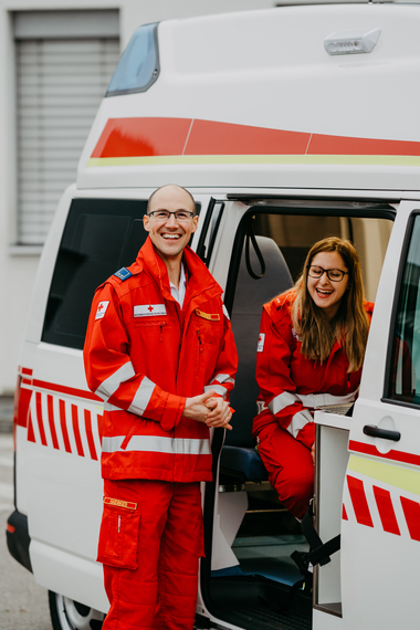 Ein Sanitäter und eine Sanitäterin lachen in die Kamera