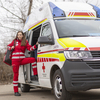 Eine junge Sanitäterin steht in der Tür eines Rettungsautos. Am Rücken trägt sie einen Notfallrucksack.