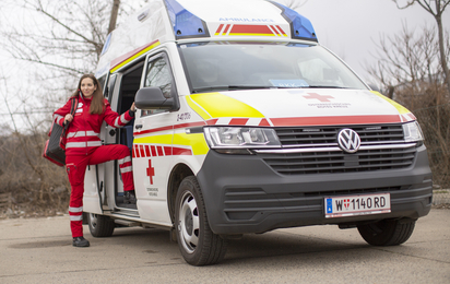 Eine junge Sanitäterin steht in der Tür eines Rettungsautos. Am Rücken trägt sie einen Notfallrucksack.