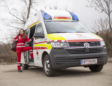 Eine junge Sanitäterin steht in der Tür eines Rettungsautos. Am Rücken trägt sie einen Notfallrucksack.