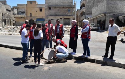 Personen schauen auf Kanaldeckel in Aleppo, Syrien