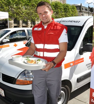 Ein junger Mann in Rotkreuz-Uniform hält ein Tablett mit Speisen in der Hand.