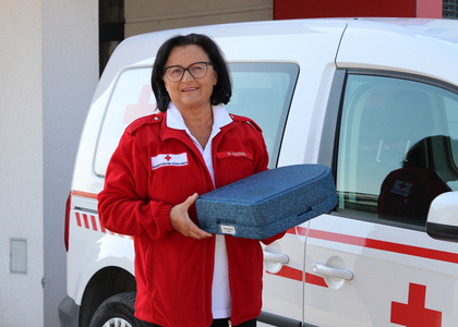 Eine Frau hält eine Essensbox in der Hand und steht vor einem Rotkreuz-Auto