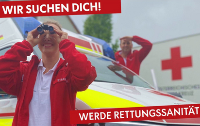 Rettungssanitäterin steht vor einem Rettungsauto und schaut durch ein Fernglas