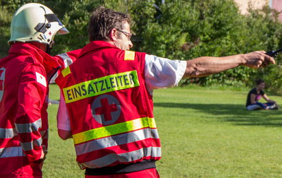 Ein Rotkreuz-Mitarbeiter mit der Rückenbeschriftung "Einsatzleiter" gibt Kommandos an einen Rotkreuz-Helfer