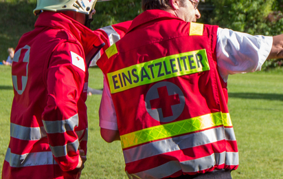 Ein Rotkreuz-Mitarbeiter mit der Rückenbeschriftung "Einsatzleiter" gibt Kommandos an einen Rotkreuz-Helfer