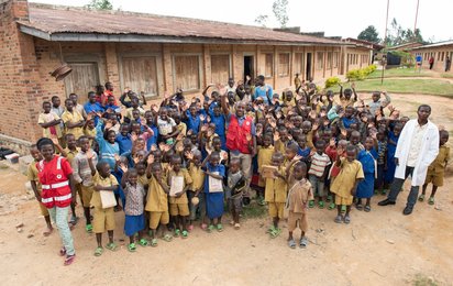 Gruppenfoto einer Schulklasse in Ruanda. Die Kinder winken begeistert in die Kamera