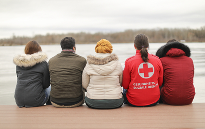 Eine Familie sitzt mit dem Rücken zu uns vor einem See.