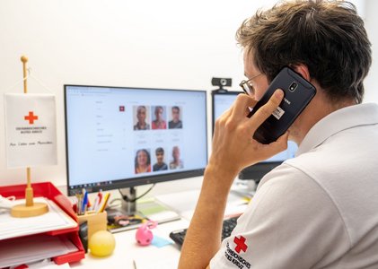 Ein Mann im Roten Kreuz Polo und von hinten zu sehen hält einen Telefonhörer und schaut in den Computer