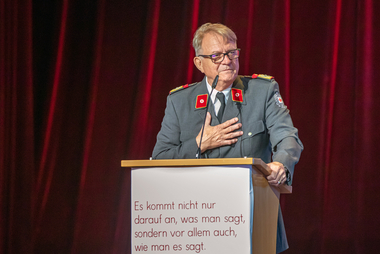 Foto einer älteren Person in Rotkreuz-Uniform, die eine Ansprache hält