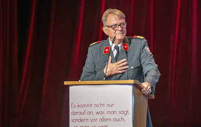 Foto einer älteren Person in Rotkreuz-Uniform, die eine Ansprache hält