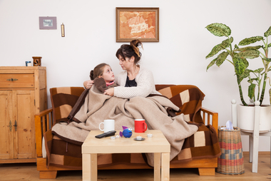 Eine Mutter sitzt mit ihrem kleinen Mädchen auf der Couch. Sie sind zugedeckt, weil die Wohnung kalt ist.