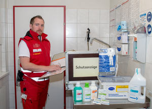 Patrick Peinhaupt - Bezirkshygienebeauftragter - steht in Rotkreuz-Einsatzuniform in einer Hygieneschleuse und stellt Equipment zur Desinfektion vor.