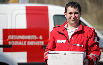 Auf dem Bild ein Rot Kreuz Mitarbeiter der Essen zustellt