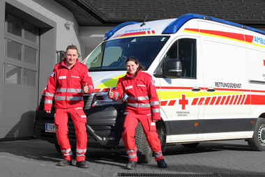 Ein RTW im Hintergrund, davor zwei Sanitäter*innen