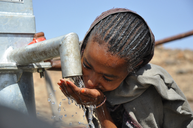 Ein Kind in Afrika labt sich am Wasserhahn. Trinkwasser für die Ärmsten der Armen