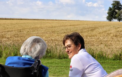 Hospizmitarbeiterin mit Klientin im Freien auf Wiese sitzend