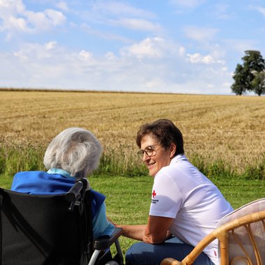 Hospizmitarbeiterin mit Klientin im Freien auf Wiese sitzend