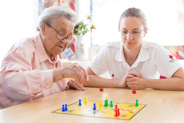 Eine ältere Dame spielt Mensch ärgere dich nicht mit einer Rotkreuz-Mitarbeiterin