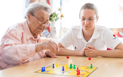 Eine ältere Dame spielt Mensch ärgere dich nicht mit einer Rotkreuz-Mitarbeiterin