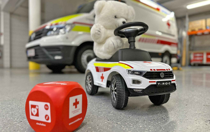 Ein weißer Teddybär sitzt auf einen Rotkreuz-Bobbycar in der Garage.