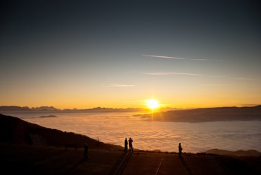 Man sieht einen farbenfrohen Sonnenuntergang, Wolken und einen Berghang.