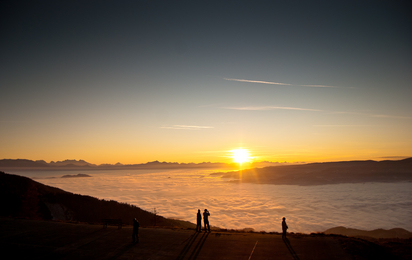 Man sieht einen farbenfrohen Sonnenuntergang, Wolken und einen Berghang.