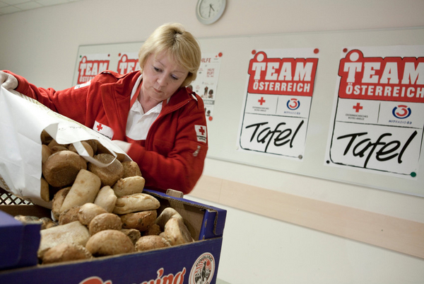 Auf dem Bild eine Dame die eine große Menge Brot in von einem Sackerl in eine Kiste leert