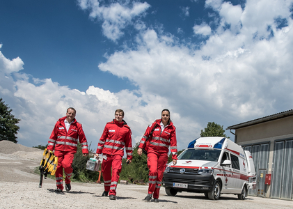 Drei Rettungssanitäter_innen gehen vom Rettungsauto auf die Kamera zu.