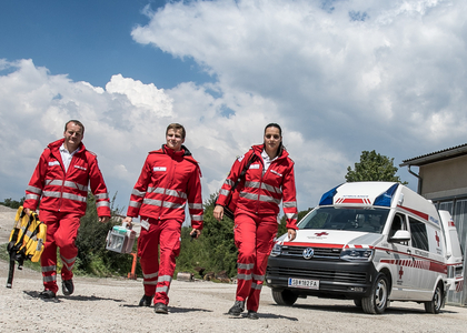 Drei Rettungssanitäter_innen gehen vom Rettungsauto auf die Kamera zu.