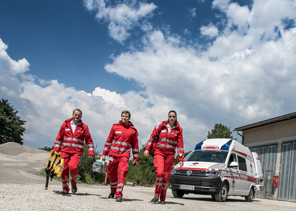 Drei Rettungssanitäter_innen gehen vom Rettungsauto auf die Kamera zu.