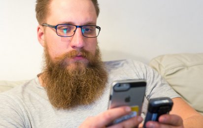 Ein junger Mann sitzt auf der Couch, hält sein Handy in der Hand und wird im Ernstfall zum Einsatz alarmiert.