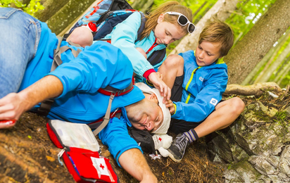 Platzwunde auf dem Kopf. Kinder leisten ihrem Vater Erste Hilfe. Sie bringen den bewusstlosen Vater in die stabile Seitenlage und verbinden die Wunde auf dem Kopf.