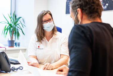 Am Bild berät eine Mitarbeiterin des Roten Kreuzes Tirol mit Maske einen Mann, der offensichtlich Migrationshintergrund hat in einem Büro