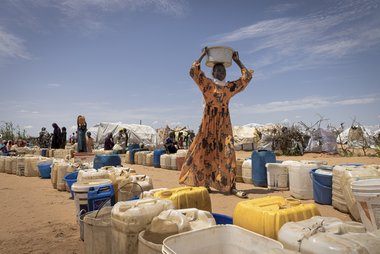 Frau aus dem Sudan trägt einen weißen Plastikübel auf dem Kopf.