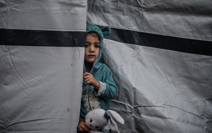 Ein kleines Mädchen in Gaza schaut vorsichtig hinter einem Zelt hervor und hält ihren schmutzigen Stoffhasen in der Hand.