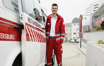 Zivildiener unterstützen das Rote Kreuz: so auch Manuel, der gerade in Uniform bereit zum Dienst neben dem Rettungswagen steht.